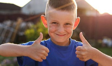 Kameraya gülümseyen ve gün batımında işaret veren genç bir adam. Gençlik ve pozitif duygu kavramı