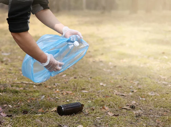 Young man collects trash plastic, glass from the ground. A volunteer cleans up the park on a sunny bright day. Clearing, pollution, ecology and plastic concept.