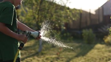 Çocuk bahçede su hortumu fıskiyesiyle oynuyor. Güneşli Yaz Günü çocukları arka bahçede oynuyor. Yavaş Çekimde