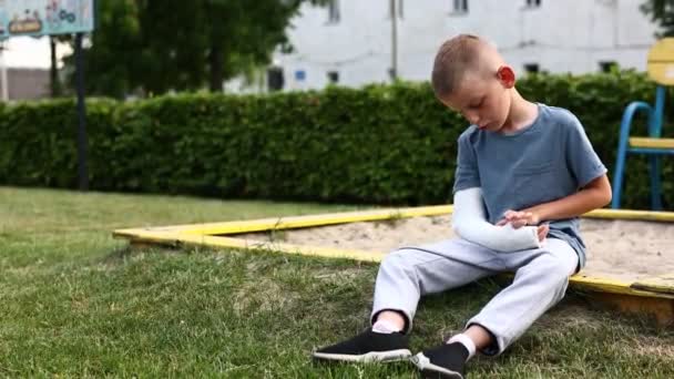 Smutny Chłopiec Złamaną Kończyną Zewnątrz Dziecko Złamaną Ręką Siedzi Przy — Wideo stockowe