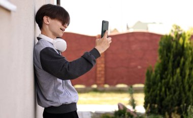 Açık havada akıllı telefon kullanan yakışıklı bir ergen. Sosyal ağlarda Çekici Genç Adam İletişim Sohbeti. Cep telefonunda müzik dinleyen öğrenci. İnsanların Boş Zamanları Konsepti.