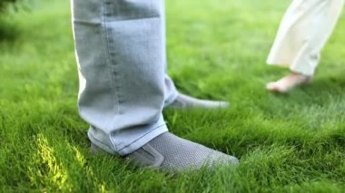 Çocuk Babalar Ayakta Duruyor. Çocuk kızın bacakları babanın ayaklarının üzerinde durur, baba da küçük kıza destek olur. Yeşil bir çayırda, doğada sevimli ayaklar