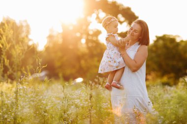 Mutlu genç anne, küçük kızıyla yaz ya da bahar güneşinde oynuyor. Bahçede ya da parkta güzel bir gün batımı ışığı. Mutlu aile kavramı