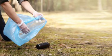 Genç adam yerden plastik ve cam topluyor. Güneşli bir günde bir gönüllü parkı temizler. Temizlik, kirlilik, ekoloji ve plastik konsept.