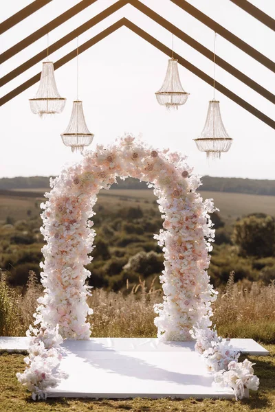 Place for wedding ceremony in garden outdoors. Wedding arch decorated with flowers and crystal chandeliers. Wedding setting. High quality photo.