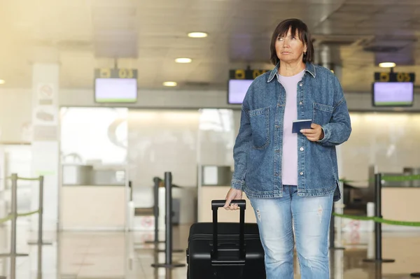 middle aged woman traveling in casual clothes. Female in airport with suitcase and passport going after check-in desk in for her flight. Passenger travel abroad on holiday or weekend