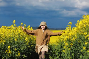 Çocuk yazın doğada eğleniyor ve koşuyor. Yağlı tohum tarlasında tatlı bir kız çocuğu. Yaz tatili konsepti.