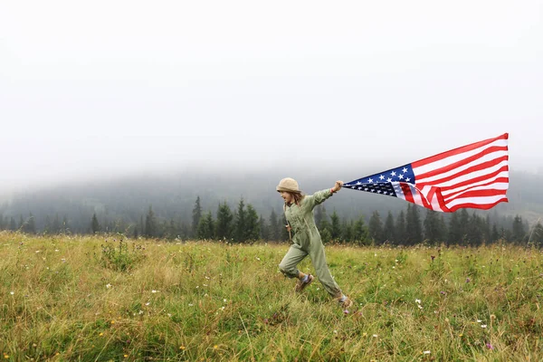 Beautiful child girl in hat with the American flag on foggy mountains. Independence Day of United States USA on 4th of July with family. Freedom. American patriotic holiday concept.
