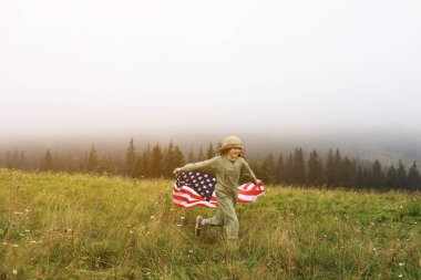 Sisli dağlarda Amerikan bayrağı taşıyan şapkalı güzel bir kız çocuğu. ABD 'nin Bağımsızlık Günü 4 Temmuz' da ailesiyle. Özgürlük için. Amerikan vatansever tatil konsepti.