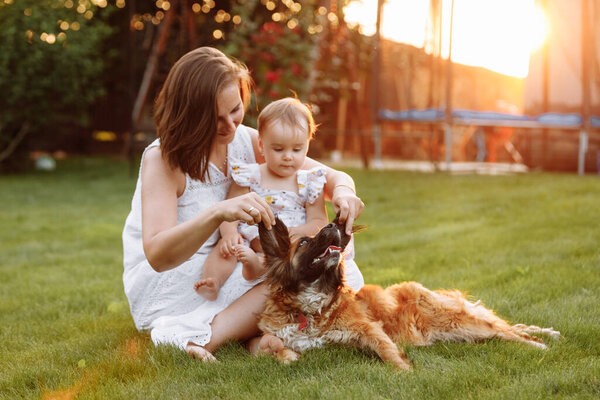 family in nature for the weekend. young beautiful mother and child girl are playing and having fun with domestic dog on backyard green grass on summer sunny day. Mothers day, baby day.