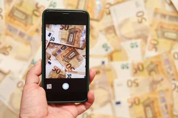 man hand takes a picture of euro banknotes on smartphone. Money paper 50 euro banknotes on the background of a smartphone screen, the concept of business, investment and income growth