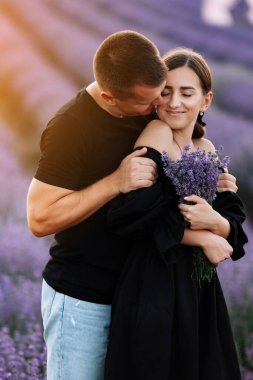 Gün batımında mor lavanta tarlasında kucaklaşan sevgi dolu çift. Güzel genç insanlar yaz sıcağında buluşur ve dışarıda birlikte yürürler. Aşk kavramı. İki kişilik genç bir aile.