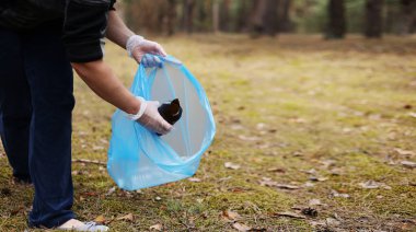 Genç adam yerden plastik ve cam topluyor. Güneşli bir günde bir gönüllü parkı temizler. Temizlik, kirlilik, ekoloji ve plastik konsept.