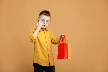 Kara Cuma 'da alışveriş. Sarı arka planda alışveriş torbaları tutan küçük bir çocuk. Bir sürü renkli kağıt torbası olan bir müşteri. Tatil satışları ve indirimler. Siber pazartesi. Yüksek kalite fotoğraf.