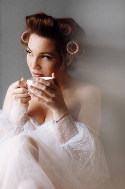 Güzellik portresi kadın. Makyajlı, beyaz elbiseli, evde dinlenen kahve ya da çay içen ve kameraya bakan güzel bir kadın. Uluslararası Kadınlar Günü.