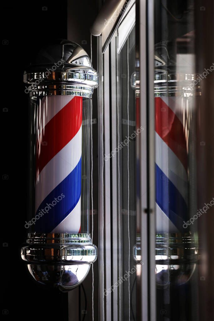 Barber pole spinning at night. International barbershop pole sign. A barber pole calling for people at street. Vintage barbershop. Salon