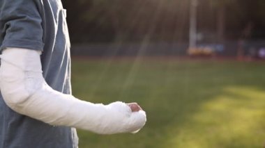 cropped shot of broken hand of child boy who greets another boy with a fist on summer day. fractured limb showing. plaster cast on the arm. Friendship. Ruined summer vacation.