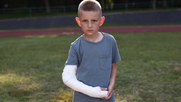 Smiling Little Boy Broken Hand Sitting Outdoors Sports Ground Summer — Vídeo de stock