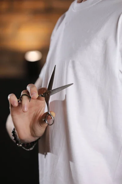 Barber in white t shirt holding scissors, background is blurred. Concept of men style. Professional tools of hairdresser. Professional occupation, art, self-care concept. Magazine. copy space.