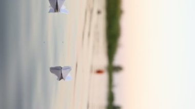 A paper boat is floating on the waves in the water at a beautiful sunset. Origami ship Sailing. The concept of a dream, future, childhood, freedom or hope. Slow motion