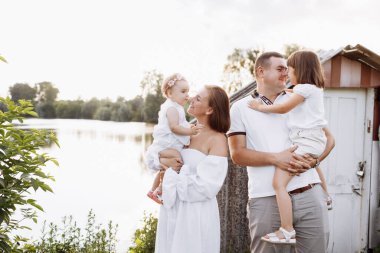 Göl kenarında mutlu genç bir aile, yazın gölet kırsalda. Anne, baba ve iki çocuk, dışarıda boş vakit geçirirken gülümsüyor ve eğleniyorlar. Aile birlikte hayattan zevk alıyor. Aile Günü
