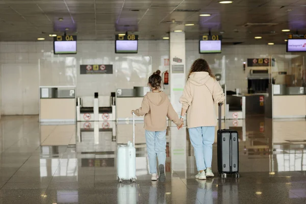 Family at airport before flight. back view of mother with daughter with suitcases going to the check-in desk for her flight. Traveling and flying with children on holiday or weekend