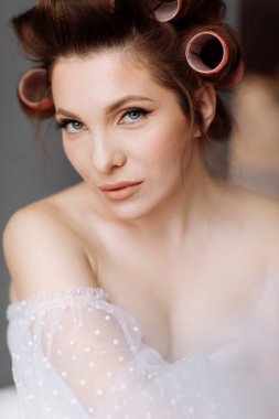 Uzun beyaz dantelli ve pembe bukleli parlak makyajlı, gösterişli, genç bir esmer kadın. Güzellik konsepti Kız gri arka planda izole edilmiş. Uluslararası Kadınlar Günü