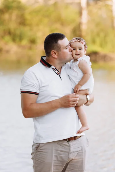 Father\'s day. Dad is hugging his baby daughter outdoors and having fun by the pond. Family enjoying life together on nature. Happy young family day. The concept of family summer holiday