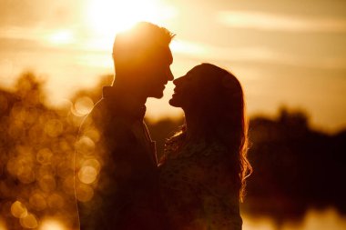 Gün batımında gölde kucaklaşan sevgi dolu çiftin silueti. Gün batımında, parlak ışıkların altında göl kıyısında yürüyen genç ve güzel bir çift. kopyalama alanı. seçici odak.