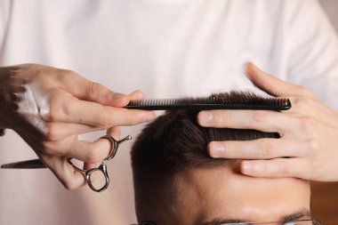 Hands of barber using scissors to cut customer's hair in salon. barber cuts hair, hairstyle. Male customer sitting in chair in hairdressing salon or barbershop. Creating new hair look