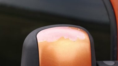faded car paint on the mirrors. Cracked and peeled paint. Close up of car side mirror. orange caf painting depreciates after long year of service. Color coating damage from aging service