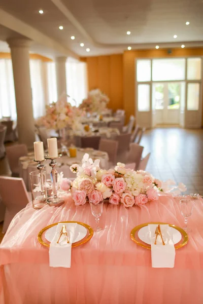 table decoration with pink tablecloth, crystal candlesticks with candles and white pink flowers in restaurant . stylish wedding day. setting table with gold plate, fork and knife.