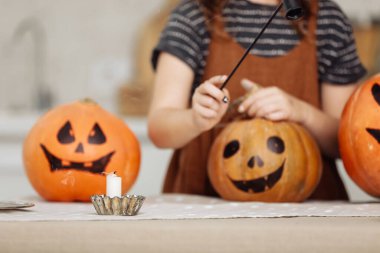 Mutlu Cadılar Bayramı. Küçük kız Cadılar Bayramı için mutfakta hazırlanıyor. Balkabağı Jack fenerleri oyulmuş gülümseme ve aile tatili için mum. Çocuk balkabaklarıyla eğleniyor.