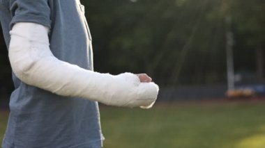 cropped shot of broken hand of child boy who greets another boy with a fist on summer day. fractured limb showing. plaster cast on the arm. Friendship. Ruined summer vacation.