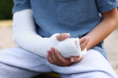 a child's arm is broken. little boy with a fractured limb outdoors. fracture injury in the summer holiday. kid is moving fingers in plaster cast on the arm
