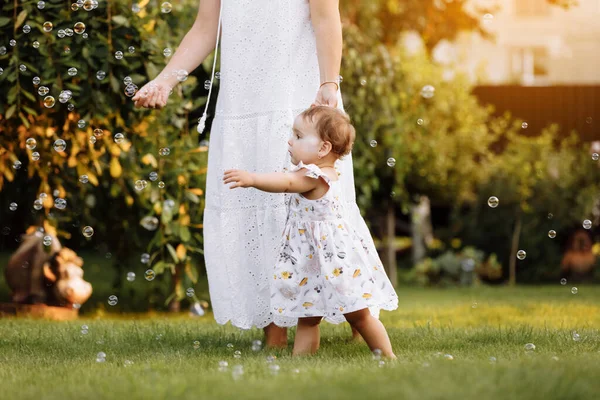 Happy Mothers Day. Young smiling mother with adorable baby daughter is having fun on backyard on summer day. Family holiday in garden. Mum and child girl walking on nature. Happy childhood. Family day