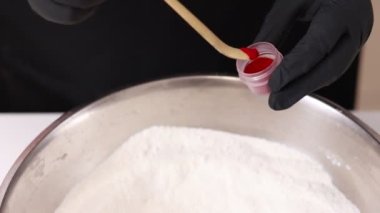 Siyah eldivenli şef pembe Fransız çörekleri için doğal kırmızı gıda boyası ya da paslanmaz kasede badem kurabiyesi fırlatır. Hamur hamuru hazırlamak için gereken malzemeler veya hamur hamuru kasesinde krema.