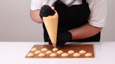 Siyah eldivenli profesyonel kadın aşçı. Makaron tatlısı için temel hazırlıyor. Kurabiye pişirmek için tepsideki boru torbasından hafif krema çıkarılmış. Pişirme, Pişirme kavramı.