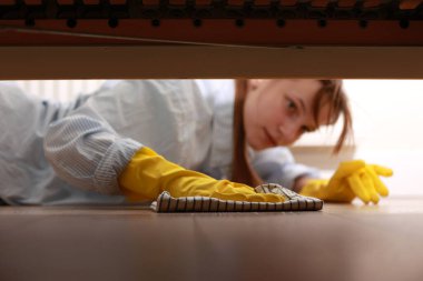 Cleaning and disinfection of surfaces. Woman with yellow rubber gloves and rag cleaning floor under bed. Beautiful woman cleaning house