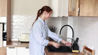young atractive woman filling drinking glass with tap water on the kitchen and drink it. Concept of clean water at home. Water quality check concept. The concept of saving, problems with water.