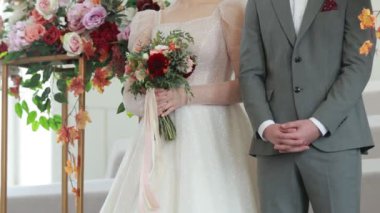 Bride in white dress and groom in grey suit on wedding ceremony. beautiful wedding bouquet in red, pink, white pastel colours and greenery in hands of bride at wedding celebration