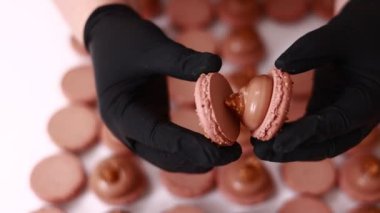 Process of making macarons macaroons, french dessert. chef hands in black gloves are assembling, connecting of two halves with chocolate stuffing at pastry shop. cooking, food and baking concept