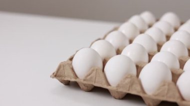 White chicken eggs in a cardboard box. Fresh raw eggs in a paper egg container for store and shop. egg tray with eggs on white table background. Top view. preparation to easter holiday.