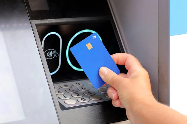 female hand with card by ATM. hand with credit card withdrawing money from ATM using NFC contactless wifi system. Wireless authentication and data transmission security in finance and banking.