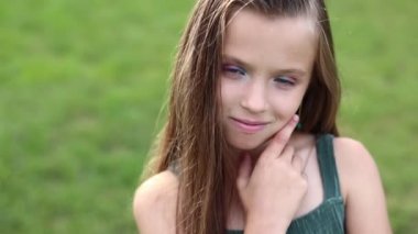 front view of adorable little girl with hairstyle is smiling with her outdoors on summer day. caucasian friendly and shy kid looking at camera posing. Happy childhood on holiday vacation.