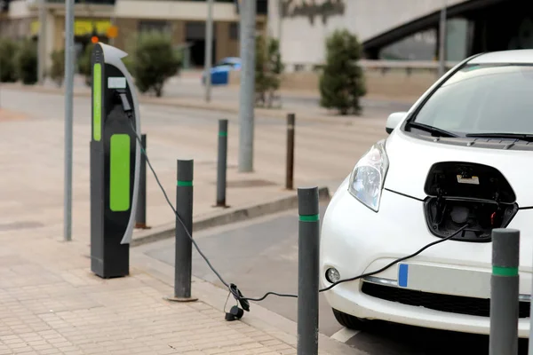 Charging modern electric cars, new energy vehicles, NEV, on the street white electric car with a cable connected and a charging station. Eco-friendly alternative energy concept.