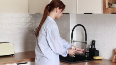 young atractive woman filling drinking glass with tap water on the kitchen and drink it. Concept of clean water at home. Water quality check concept. The concept of saving, problems with water.
