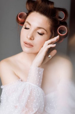 Uzun beyaz dantelli ve pembe bukleli parlak makyajlı, gösterişli, genç bir esmer kadın. Güzellik konsepti Kız gri arka planda izole edilmiş. Uluslararası Kadınlar Günü