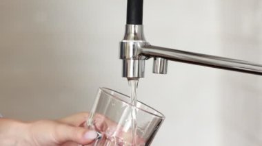 Woman filling drinking glass with tap water on the kitchen. Concept of clean drinking tap water at home. Pouring fresh drink. Water quality check concept. The concept of saving, problems with water.