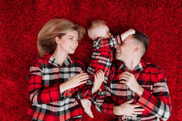 Happy Young Parents Baby Boy Same Pyjamas Lying Red Floor — Stok fotoğraf